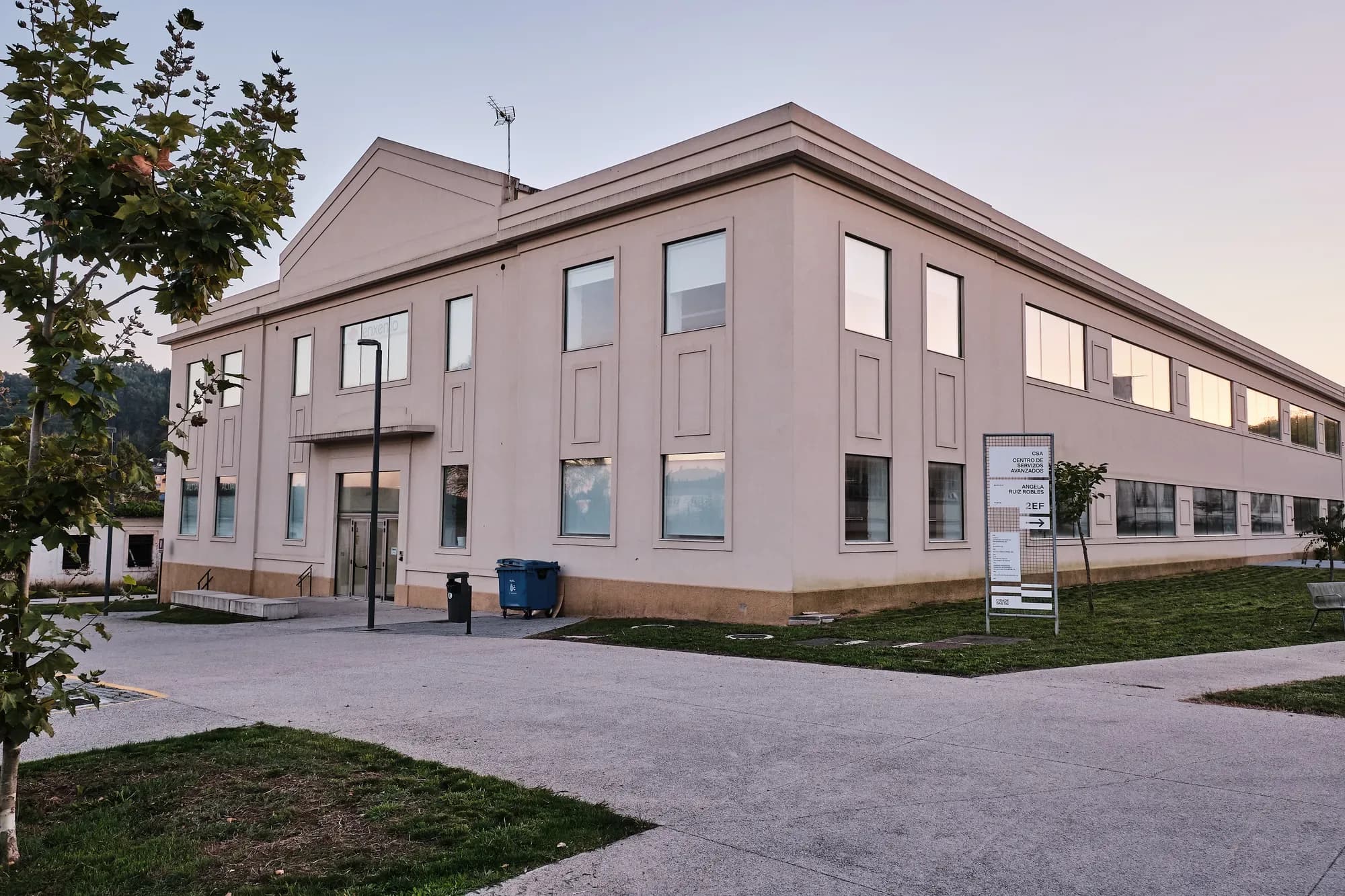 Entrada do edificio na fachada do frontón: porta de vidro baixo unha pequena marquesiña e, á dereita, sobre o céspede, o tótem «CSA · Centro de Servizos Avanzados · Angela Ruiz Robles · 2EF».