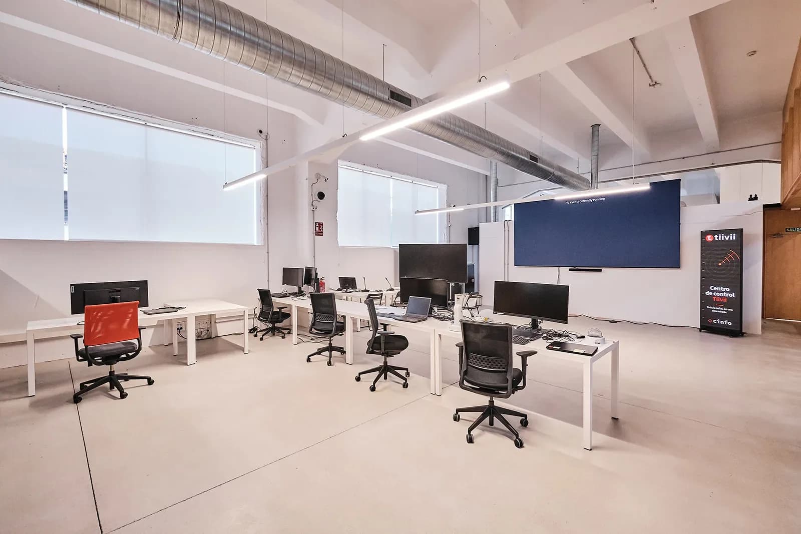 Laboratorio de medios: fila de postos con monitores, portátiles e cadeiras de oficina, unha delas laranxa, fronte a unha gran pantalla LED azul e un tótem «Centro de control Tiivii».