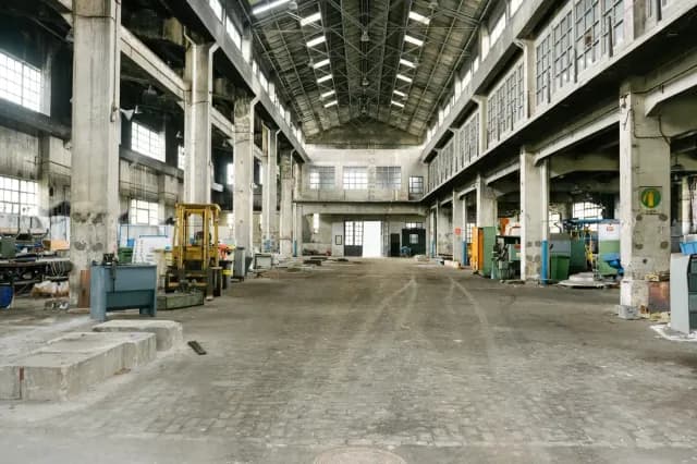 Interior dunha gran nave industrial da Fábrica de Armas antes da obra, cos seus piares de formigón e maquinaria residual.